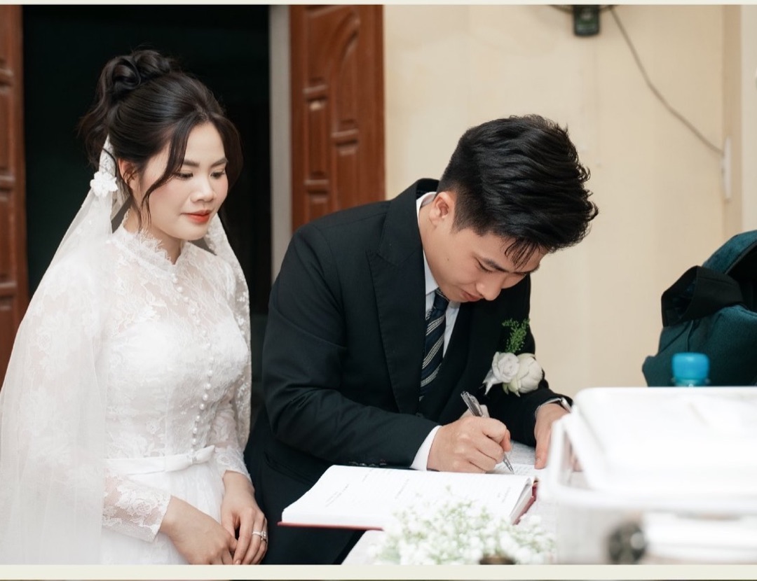 Chú rể ký tên vào sổ hôn phối của giáo xứ, cô dâu đứng bên cạnh