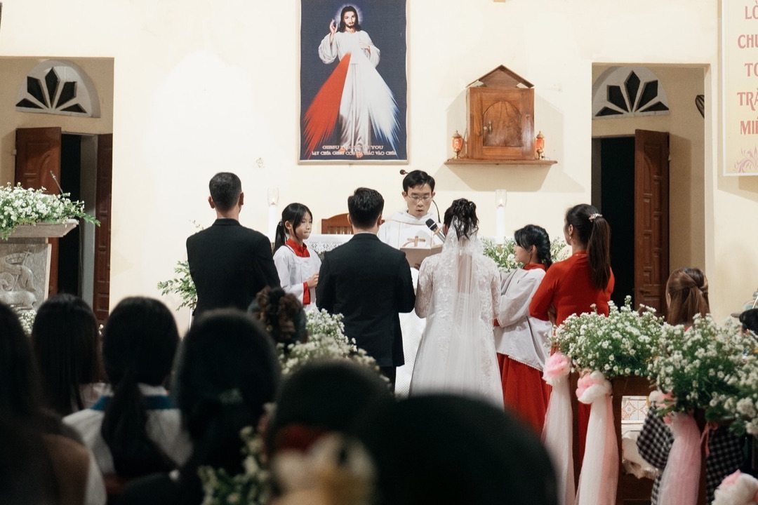 Toàn cảnh nghi thức hôn phối trước cung thánh, linh mục chủ sự đứng giữa đôi tân hôn và cộng đoàn dự lễ phía dưới